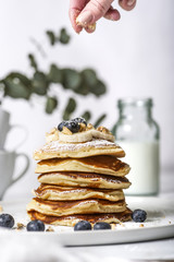 Pile of american pancakes with blueberries. A woman's hand sifting it with powdered sugar.
