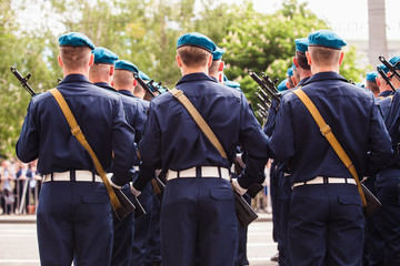 Military in the blue dress uniform and blue berets with guns standing with his back to the viewer