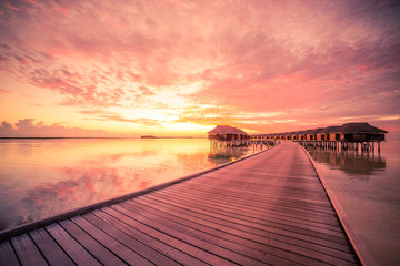 Naklejka na ściany i meble Sunset on Maldives island, luxury water villas resort and wooden pier. Beautiful sky and clouds and beach background for summer vacation holiday and travel concept