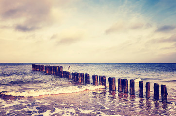 Vintage toned picture of an old wooden breakwater on a beach at sunset.