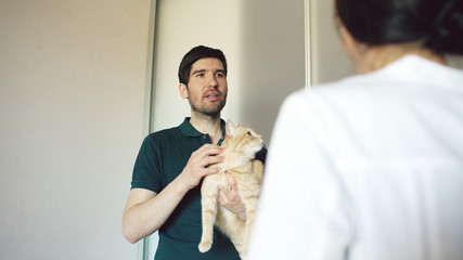 Cat owner man talking with vet woman in veterinarian office