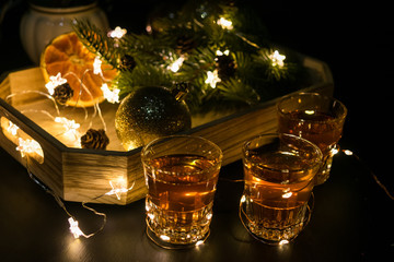 New Year Party decoration with alcohol shot glasses. Toned. Spruce tree, oranges, lights, garlands.