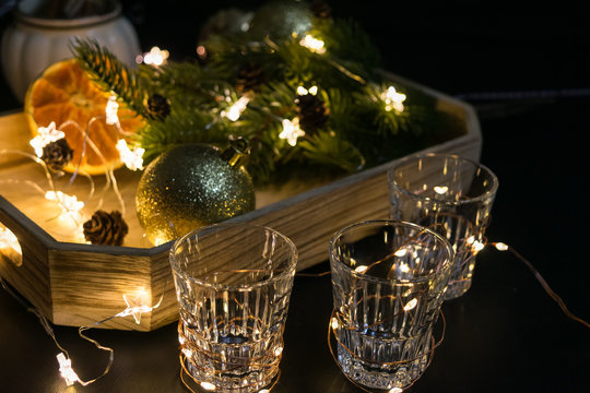 New Year Party decoration with alcohol shot glasses. Toned. Spruce tree, oranges, lights, garlands.