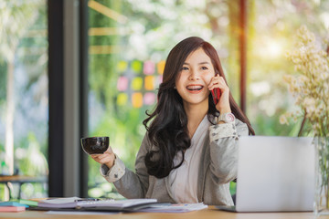 Young Asian female entrepreneur talking on the phone while working at home office.