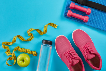 Sneakers with measuring tape on cyan blue background. Centimeter in yellow color, pink sneakers, dumbbells and bottle of water, copy space.