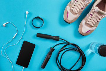 Flat lay shot of Sport equipment. Sneakers, jump rope, earphones and phone on blue background.