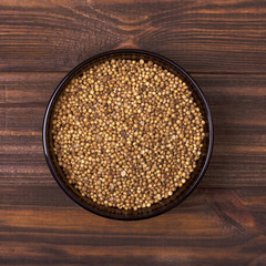 Coriander seeds in a bowl on a wooden background