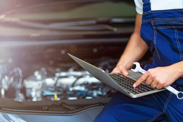 Mechanic Using Laptop While Examining Car Engine
