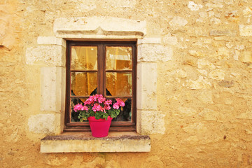 Outdoor stone wall, wooden window, pink geraniums in pot on window sill