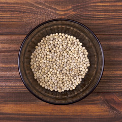 White pepper in a bowl on a wooden background