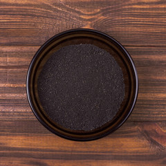 Black cumin powder in a bowl on a wooden background