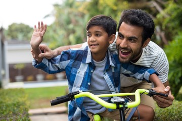 Father and son waving hand while cycling