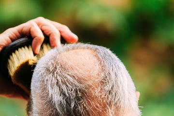Close-up of a gray-haired man combing himself with a bristle brush