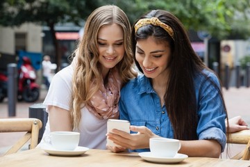 Happy friends drinking coffee while using smart phone at