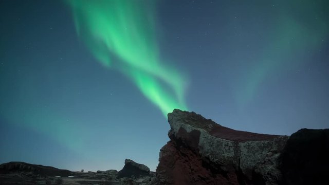 Aurora borealis swirling over moonlit jagged volcanic terrain Iceland
