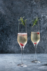 Two glasses of white champagne served with red berries and rosemary over blue texture background. Copy space