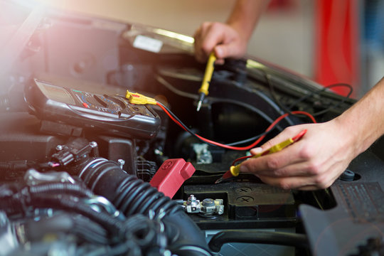 Auto mechanic checking car battery voltage
