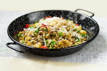 Risotto from indian rice with vegetable (pepper, pea) sprinkled with cheese in rustic black spotted pan .