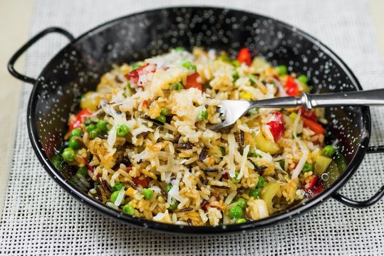 Risotto with vegetable (pepper, pea) sprinkled with cheese in rustic pan.