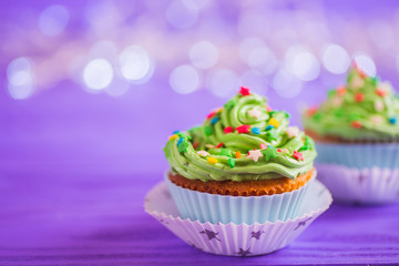 Two cupcakes with creamy green top with colorful stars and sprinkles on purple bokeh background