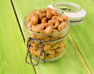 glass jar with cashew nuts and green wooden background, side view