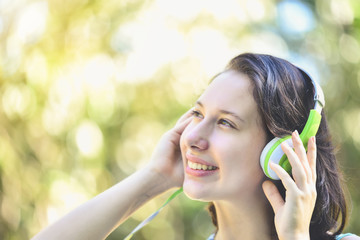 Beautiful women are listening to music with their eyes closed, and white,green headphones are relaxing and happy in the garden amid green bushes.