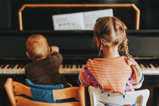 Two Little Kids Playing On Piano, Toddler Girl And Baby Boy Practicing Music At Home, Back View