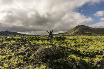 person standing on rock with raised hands and looking at scenic icelandic landscape