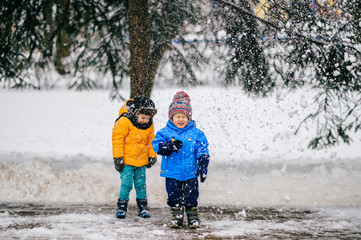 Fototapeta na wymiar Happy funny children laughing under falling snow. Kids friends have fun under tree in winter park outdoor at nature. Two handsome young boys have snowy party with emotional faces. Sincere male fellows