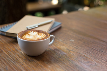 Cup of hot coffee with milk art and notebook on the wooden table.