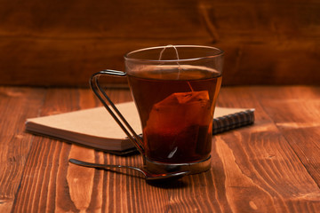 Tea and notebook on wooden background. Glass of black tea