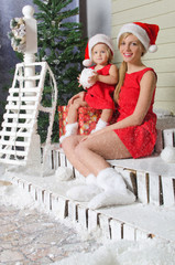 Mom and daughter in Santa's suits are sitting under snow