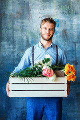 Male florist holding wooden box with flowers on blue background