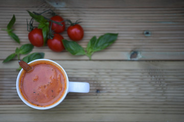 food photography image of home made tomato and herb soup in a white mug with fresh basil leaves on a rustic wood background with space
