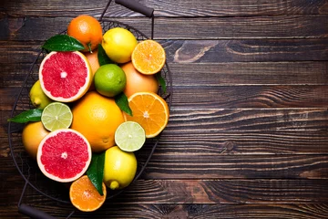 Foto op Plexiglas Fresh citrus fruits in basket. Orange, grapefruit, lemon, lime, tangerine on dark wooden table. Assorted fresh citrus fruits with leaves. Top view and copy space © missmimimina