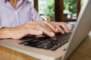 Senior woman typing on laptop at table in cafe shop