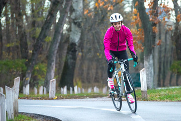 Fototapeta premium Young Woman in Pink Jacket Riding Road Bicycle in the Park in the Cold Autumn Day. Healthy Lifestyle.