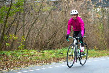 Naklejka premium Young Woman in Pink Jacket Riding Road Bicycle in the Park in the Cold Autumn Day. Healthy Lifestyle.