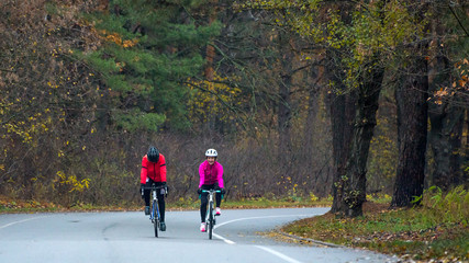 Two Young Female Cyclists Riding Road Bicycles in the Park in the Cold Autumn Morning. Healthy Lifestyle.