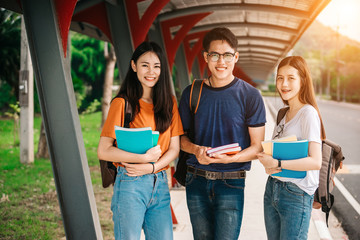 A group of young or teen Asian student in university smiling and reading the book and look at the tablet or laptop computer in summer holiday.