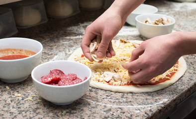 Cook in the kitchen putting the ingredients on the pizza. Pizza concept.