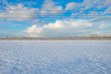 Railway through a snowy field in sunlight in winter