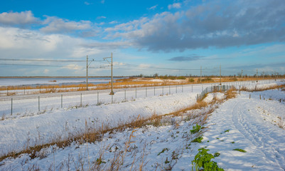 Railway through a snowy field in sunlight in winter