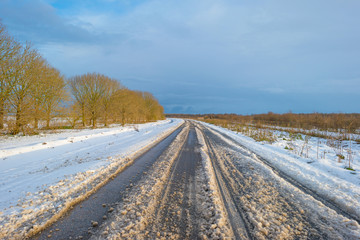 Fototapeta na wymiar Snowy road through a frozen landscape along trees in winter