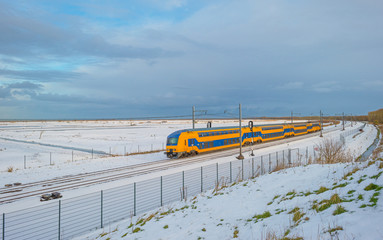 Train riding through a snowy field in sunlight in winter