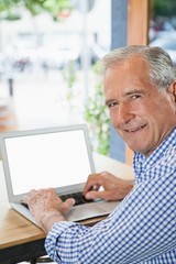 Happy senior man using digital laptop while sitting at cafe shop