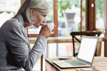 Side view of senior woman drinking coffee while using laptop