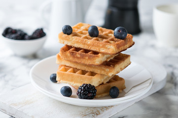 Waffles on a white plate decorated with blueberries with marbled background. copy space