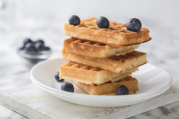 Waffles on a white plate decorated with blueberries with marbled background. copy space
