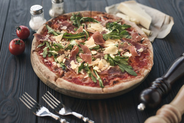 close up view of italian pizza, cutlery and ingredients on wooden